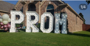 Large illuminated marquee letters spelling "PROM" set up in front of an elegant Dallas residence home, creating a glamorous entrance for a pre-dance photoshoot. Rented from Dallas Event Rentals.