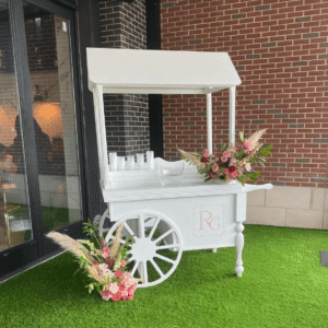 An elegant white candy cart filled with glass jars of colorful candies at a stylish Dallas wedding, with guests enjoying sweet treats. Rented from Dallas Event Rentals.
